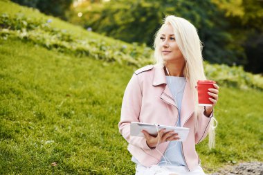 Gülümseyen yakışıklı kadın onun cep telefonu ya da tablet vasıl belgili tanımlık park Kulaklığımda rahatlatıcı müzik dinlemek. Bir öğrenci için bir online ders dinler ve sınavları için hazırlar. yalnızlık zevk kız