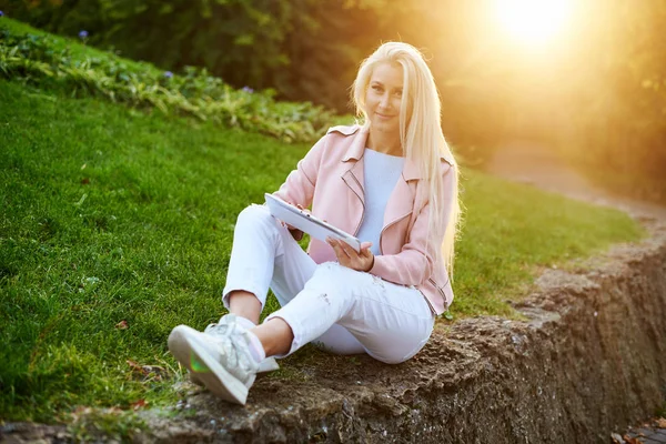 Smiling handsome woman listening relaxing music In the headphones  with her mobile phone or tablet at the park. A student listens to an online lecture and prepares for exams. girl enjoying loneliness