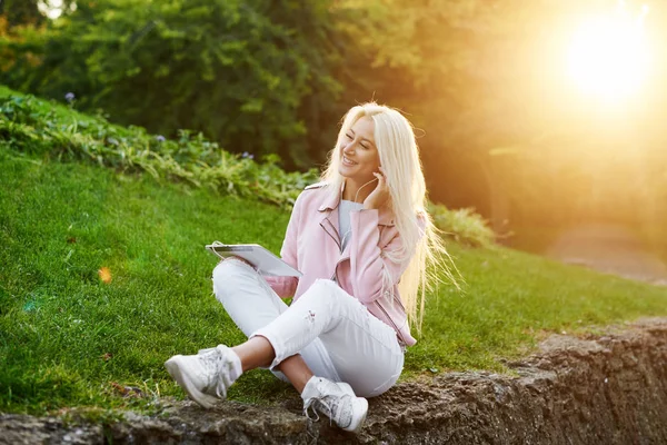 Smiling handsome woman listening relaxing music In the headphones  with her mobile phone or tablet at the park. A student listens to an online lecture and prepares for exams. girl enjoying loneliness