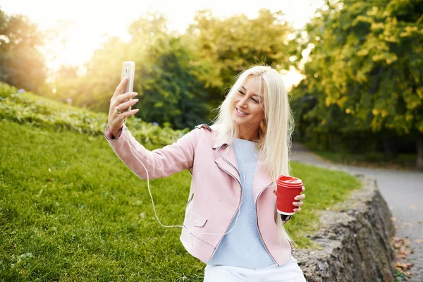 스마트폰 이어폰에서 음악을 귀여운 여자는 공원에는 Selfie를 걸립니다 그녀는 — 스톡 사진
