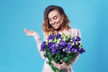Buket üzerinde mavi arka plan izole mor bahar çiçek tutan genç mutlu gülümseyen Kızıl saçlı kadın. Kadın 8 Mart gününde veya doğum günü onuruna şenlikli buket