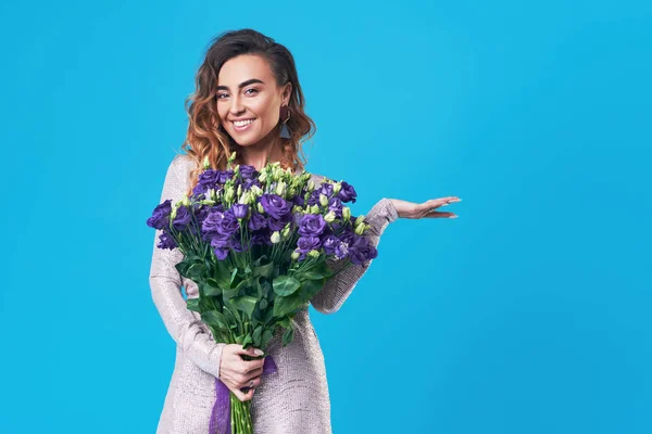 stock image Young happy smiling redhead woman holding bouquet of violet spring flowers isolated on blue background. Festive bouquet in honor of women's day on March 8 or birthday