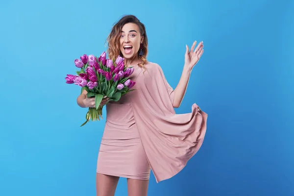 Young happy smiling redhead woman holding bouquet of colorful spring flowers isolated on blue background. Pink tulips, festive bouquet in honor of women\'s day on March 8 or birthday