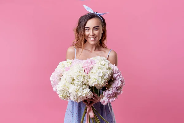 Cheerful young lady in retro round glasses being excited to get bouquet of blue spring flowers on women\'s day isolated over pink background. It is looking to the right, space for text