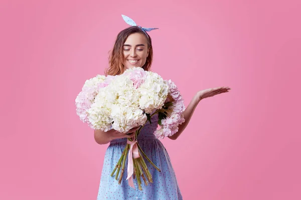 Cheerful young lady in retro round glasses being excited to get bouquet of blue spring flowers on women\'s day isolated over pink background. It is looking to the right, space for text
