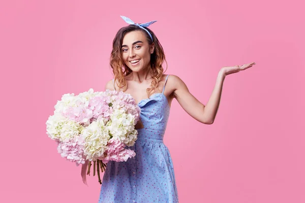 Cheerful young lady in retro round glasses being excited to get bouquet of blue spring flowers on women's day isolated over pink background. It is looking to the right, space for text