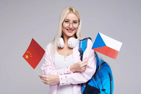 Education, foreign language translator, english, student - smiling blond woman in headphones holding China and Czech Republic flags. Distance learning