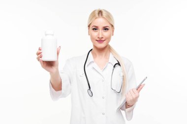 Beyaz arka plan üzerinde izole beyaz hap şişe işaret stetoskop ile çekici genç bir kadın doktor