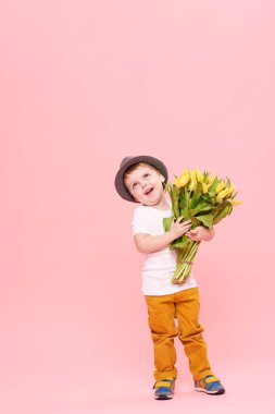 Bahar çiçek buketi pembe üzerinde izole kamera bakıyor tatlı gülümseyen hamile. Anne için hediye olarak Sarı laleler tutan şapkalı küçük yürümeye başlayan çocuk