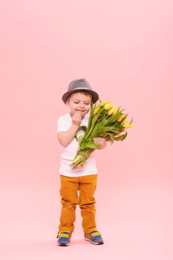 Bahar çiçek buketi pembe üzerinde izole kamera bakıyor tatlı gülümseyen hamile. Anne için hediye olarak Sarı laleler tutan şapkalı küçük yürümeye başlayan çocuk