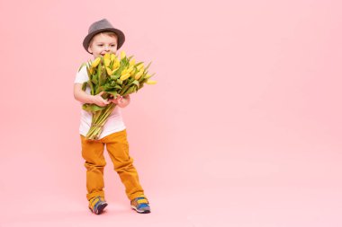 Bahar çiçek buketi pembe üzerinde izole kamera bakıyor tatlı gülümseyen hamile. Anne için hediye olarak Sarı laleler tutan şapkalı küçük yürümeye başlayan çocuk