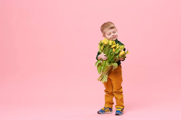 春花の花束ピンクに分離カメラ目線で愛らしい笑顔の子 小さな幼児男の子のお母さんのためのギフトとして黄色のチューリップを保持しています 左側にテキスト用のスペースをコピーします — ストック写真