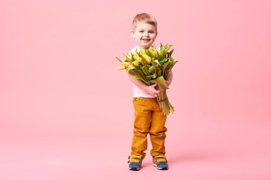 Bahar çiçek buketi pembe üzerinde izole kamera bakıyor tatlı gülümseyen hamile. Küçük yürümeye başlayan çocuk için anne hediye olarak Sarı laleler holding. Metin için yer kopyalayın 
