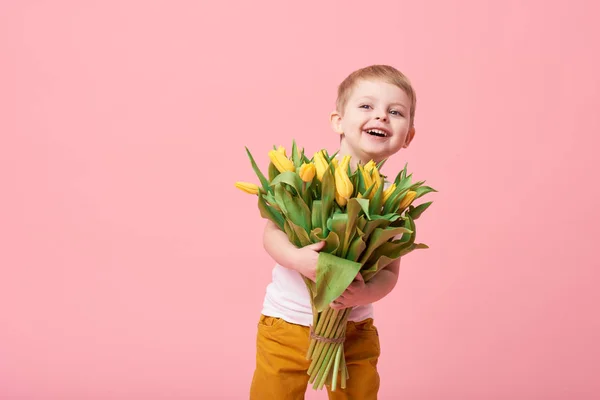 春花の花束ピンクに分離カメラ目線で愛らしい笑顔の子 小さな幼児男の子のお母さんのためのギフトとして黄色のチューリップを保持しています コピーのテキストのための領域 — ストック写真