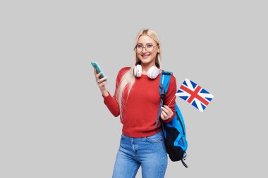 Online Eğitim, yabancı dil çevirmen, İngilizce, öğrenci - gülümseyen hareket eden telefon ve İngiliz bayrağı tutarak Kulaklığımda sarışın kadın. Uzaktan eğitim
