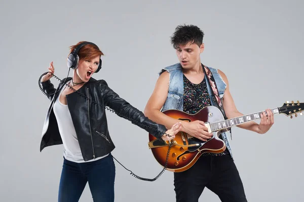 Musical artists sing and play electric guitar. Contemporary cover band. Isolated over grey background. Woman and man with headphones sing loudly