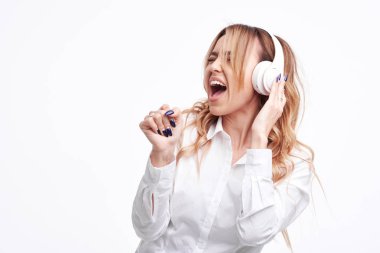 Wireless connection. Portrait of young beautiful pleasure woman listening music with headphones and singing loudly, posing isolated over white background,  