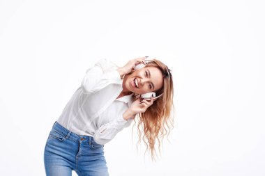 Kulaklıkta radyoda yüksek sesle komik müzik dinleyen genç kadın. Rahat giysiler içinde mutlu kız saç sallayarak ve gülüyor ile poz. beyaz stüdyo arka planda eğlenmek