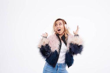 beautiful redhead woman in fur coat and white headphones listens to music and dancing on white isolated background
