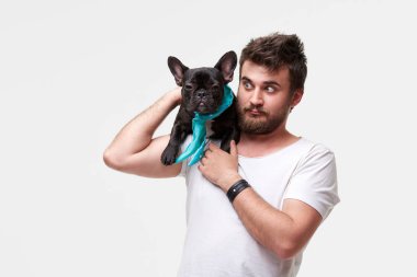 Hipster Sakallı adam tutan ve sevgi ile kollarında güzel bir Fransız Bulldog köpek sarılma ve onunla oynarken, gri bir arka plan karşı