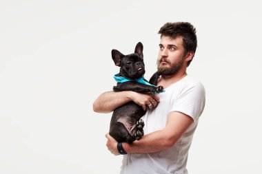 Hipster Sakallı adam tutan ve sevgi ile kollarında güzel bir Fransız Bulldog köpek sarılma ve onunla oynarken, gri bir arka plan karşı