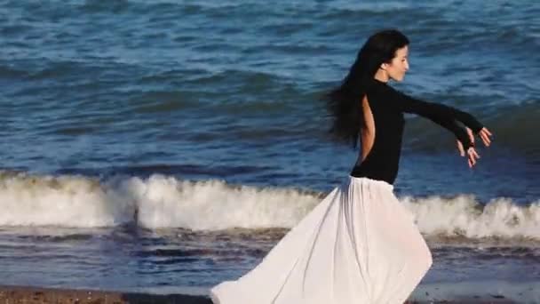 快乐的黑头发女孩在夜晚的海滩上优雅地跳舞 在明亮的阳光下 在泡沫的海浪下慢动作 — 图库视频影像