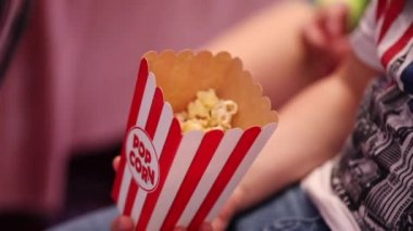 çocuk el snack ile büyük beyaz ve kırmızı kağıt kutu tutar ve sinema aşırı yakın görünümünde film izlerken patlamış mısır yiyor