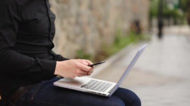 siyah gömlek ve kot pantolon türleri ağ saldırı görevi akıllı telefon üzerinde dizüstü bilgisayar üzerinde diz yakın görünüm üzerinde tutarak hacker