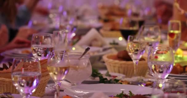 パーティーの極端な近いビューで座って食べているぼやけた人々に対してテーブルの上に水とワインと透明なグラス — ストック動画