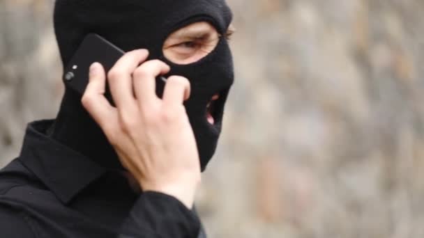 情绪愤怒的罪犯在黑色防盗面具和衬衫谈话在现代电话大致慢动作近距离观看 — 图库视频影像