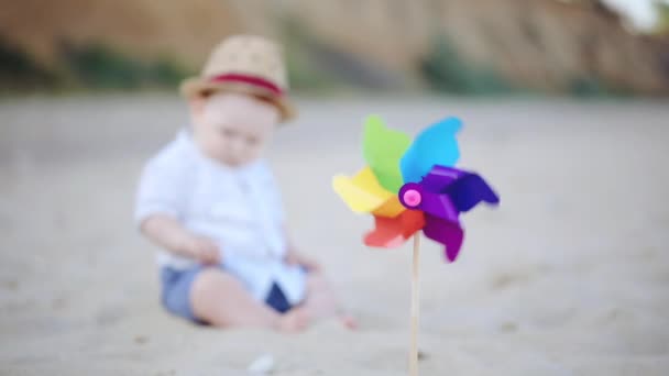 模糊的幼儿在棕色草帽剪影在沙滩上玩 风车在前景慢动作 — 图库视频影像