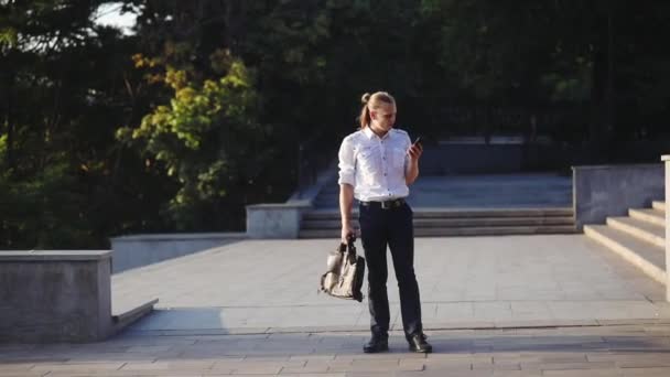 Молодой Человек Рубашке Хвостиком Смотрит Телефон Радостно Танцует Против Ступенек — стоковое видео