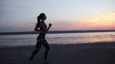 sportif genç kadın nefes kesen günbatımı gökyüzü yavaş hareket karşı deniz plajında kardiyo egzersiz ve jogs uygulamaları