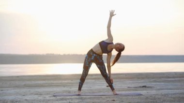 at kuyruğu ile konsantre bayan deniz yakın görünümü yavaş hareket sahilde ayakta germe yoga pozisyonları gerçekleştirir