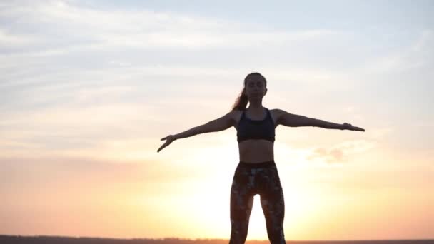 熟練した若い女性は 幻想的な夕日の裏側の景色に対して頭の上に手をつなぐヨガの呼吸技術を練習します — ストック動画