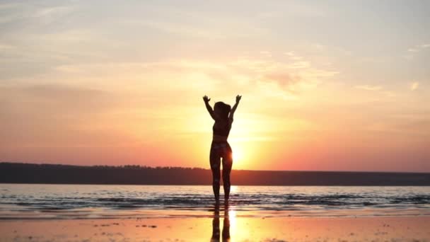 ポニーテールを持つ女性は 腕を広げ 幻想的な夕日の裏側スローモーションに対して海で体の筋肉を伸ばします — ストック動画