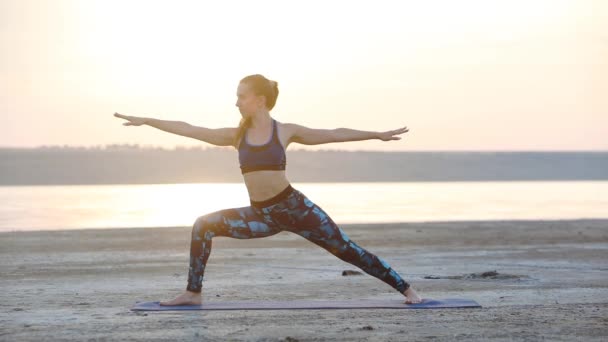 年轻女子与完美的身体练习瑜伽战士Asana把垫子在湿沙海滩近距离观察慢动作 — 图库视频影像