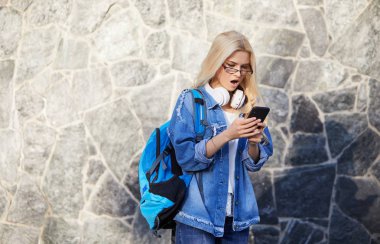 Endişe korkmuş genç kadın öğrenci portresi duvar arka planda kötü haber veya fotoğraf görünce telefon bakıyor. Olumsuz duygular. İnsan reaksiyonu, ifade ve teknoloji konsepti