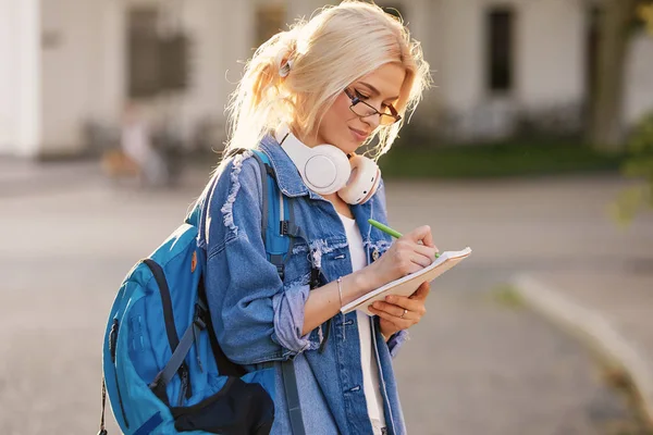 Genç yetenekli kadın öğrenci rahat giyim şehir etrafında yürüyüş giyinmiş ve kulaklıklar üzerinden radyo dinleme. Çekici esmer kadın gitmek ve mobil ile açık havada ücretsiz zaman zevk kahve almak