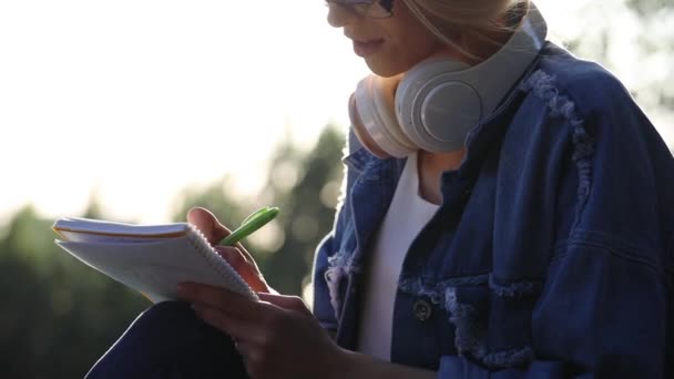 Flicka i denim jacka skriver i anteckningsbok med grön penna nära — Stockvideo