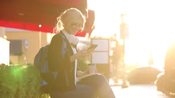 Lady med kaffekopp sitter på betong bröstvärn och typer — Stockvideo