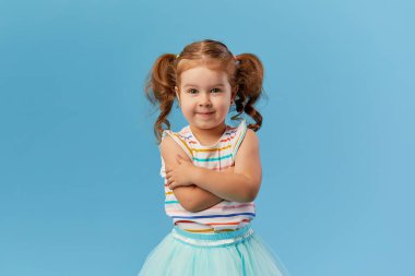 Mavi arka planda izole şirin küçük Toddler kız çocuk ayakta gülümseme portre. Kameraya bakıyor. 