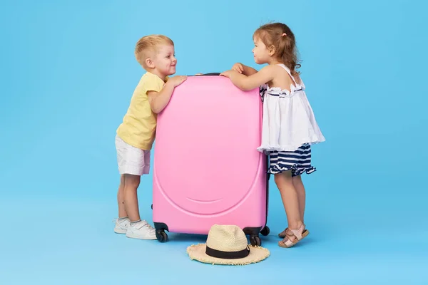 快乐的孩子拿着五颜六色的粉红色手提箱准备暑假 年轻的旅行者小女孩和男孩 妹妹和弟弟 有乐趣孤立在蓝色背景 — 图库照片