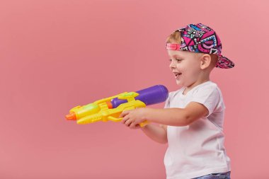 Pembe duvar arka planda oyuncak su tabancası tutan yaz giysileri mutlu küçük yürümeye başlayan çocuk
