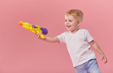 Pembe duvar arka planda oyuncak su tabancası tutan yaz giysileri mutlu küçük yürümeye başlayan çocuk