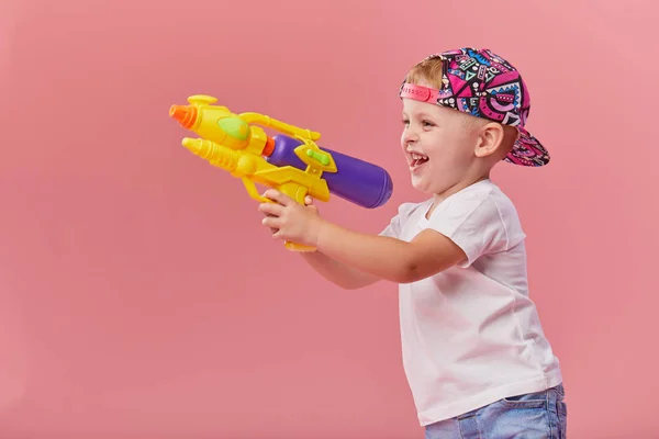 Pembe duvar arka planda oyuncak su tabancası tutan yaz giysileri mutlu küçük yürümeye başlayan çocuk