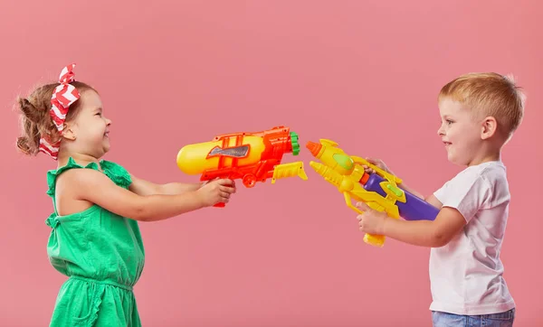 ピンクの壁の背景におもちゃの水の銃を保持夏の服で幸せな小さな幼児の男の子と女の子 — ストック写真
