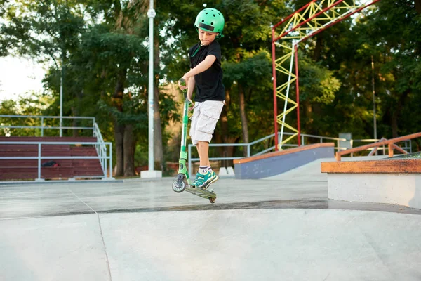 A boy on a scooter and in protective helmet do incredible stunts in skate park. Extreme jump. The concept of a healthy lifestyle and sports leisure