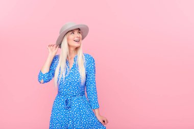 Yaz şapka ve şık mavi elbise ve pembe arka plan üzerinde izole parantez içinde gülümseyen çekici sarışın kadın Portresi. Sağlıklı ve kar beyazı bir gülümseme kavramı. Sağdaki metin için alan