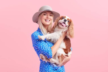 Şapkalı genç kadının pembe arka planda köpeğine sarıldığı portresi
